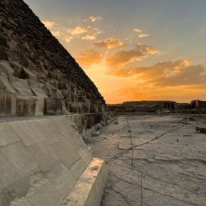 edge of pyramid with sun setting in distance among puffy white clouds